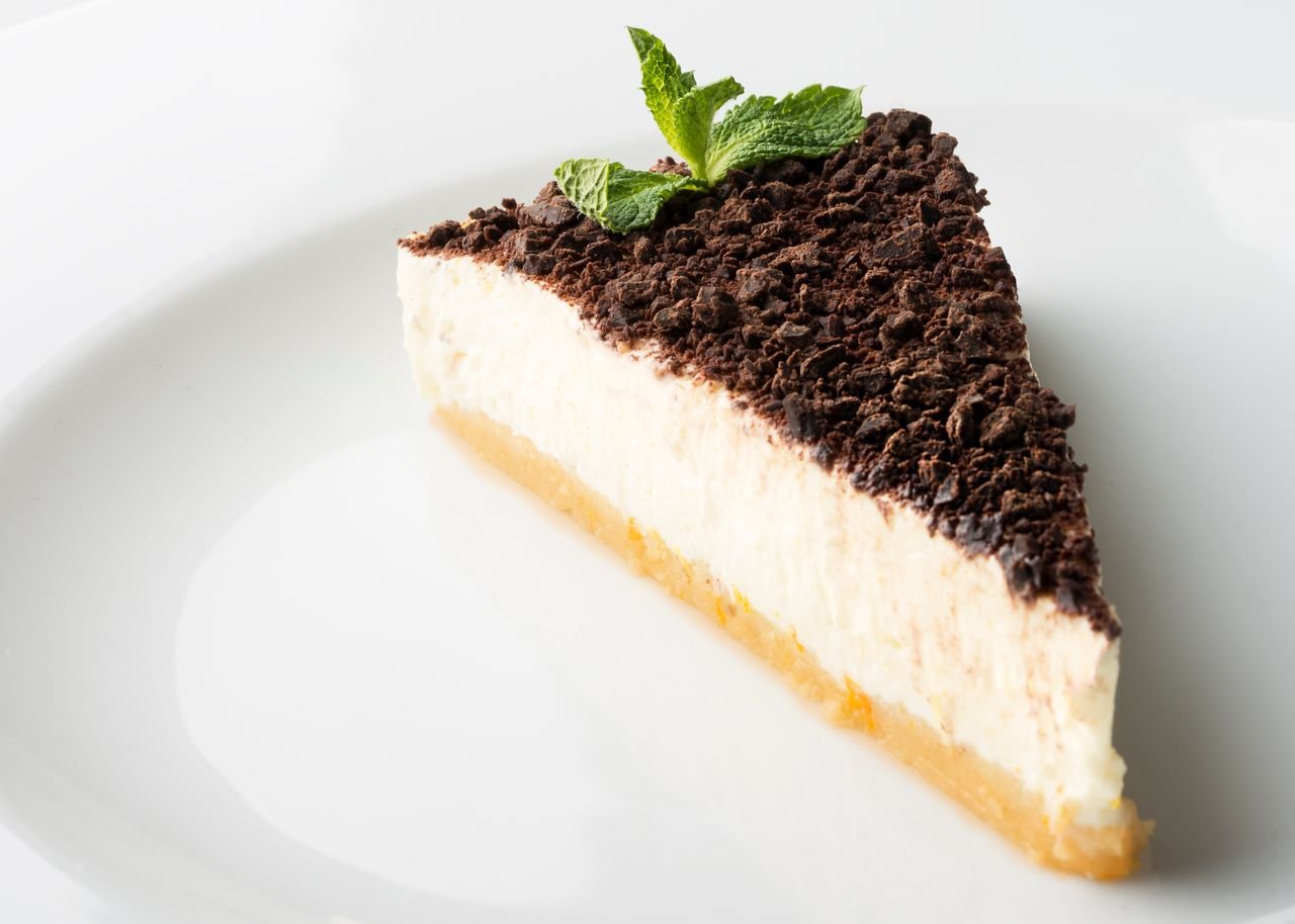 A mouthwatering slice of cheesecake topped with chocolate and mint on a white plate.