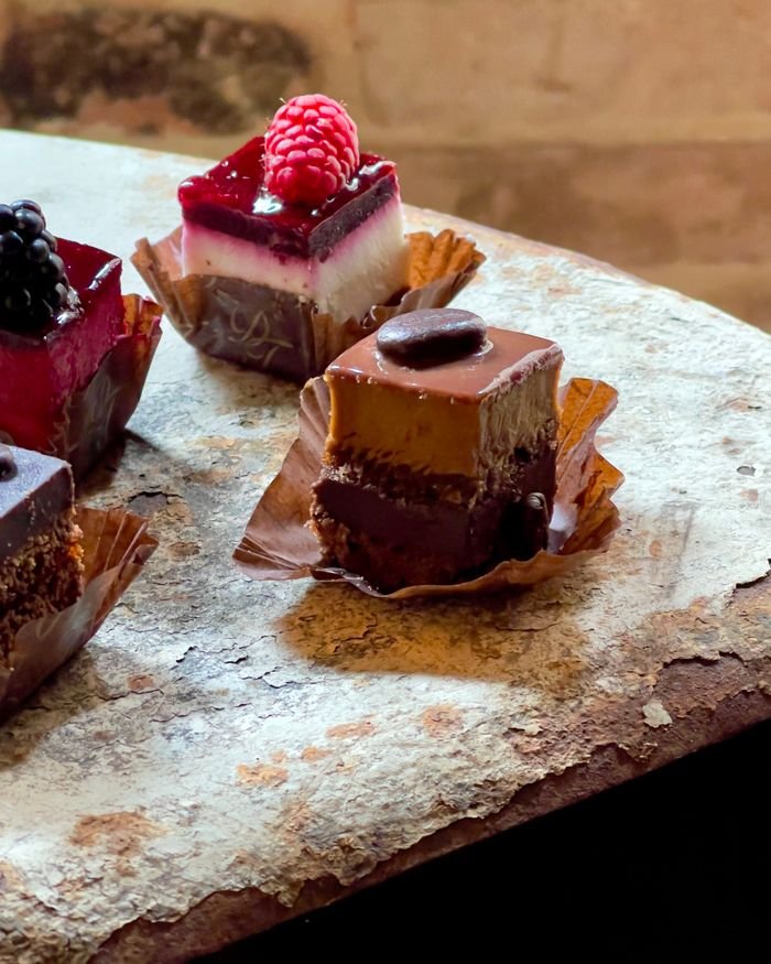 quality-assurance-02 A tempting assortment of mini cakes with chocolate and berry toppings on a rustic wooden surface.