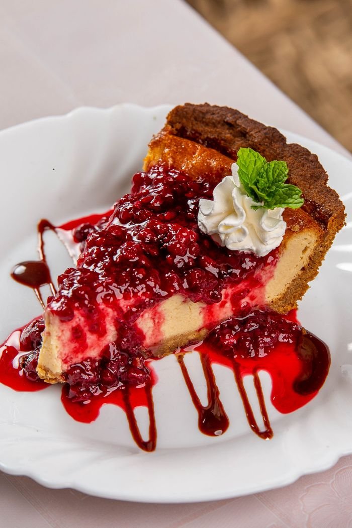 A delectable slice of cheesecake topped with juicy raspberry sauce and a mint garnish.
