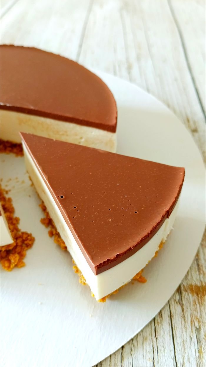A close-up of a slice of chocolate-topped cheesecake on a rustic wooden table.