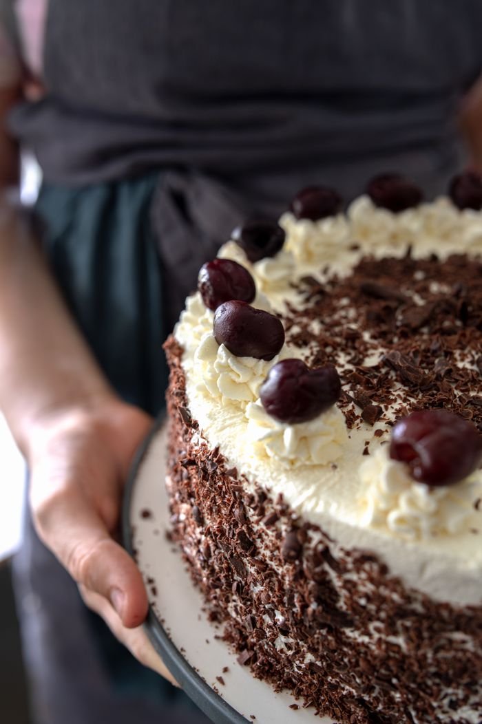 social-feed-img-01 Close-up of a Black Forest cake topped with cherries and whipped cream.