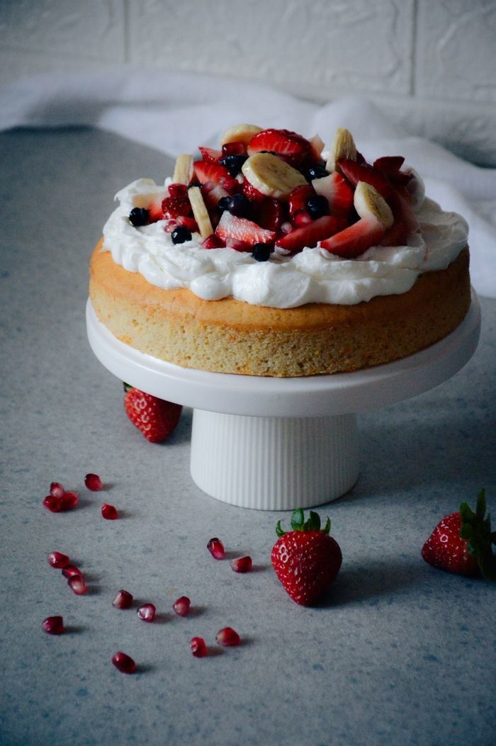 social-feed-img-03 A delectable cake garnished with fresh fruit on a white stand, inviting and scrumptious.
