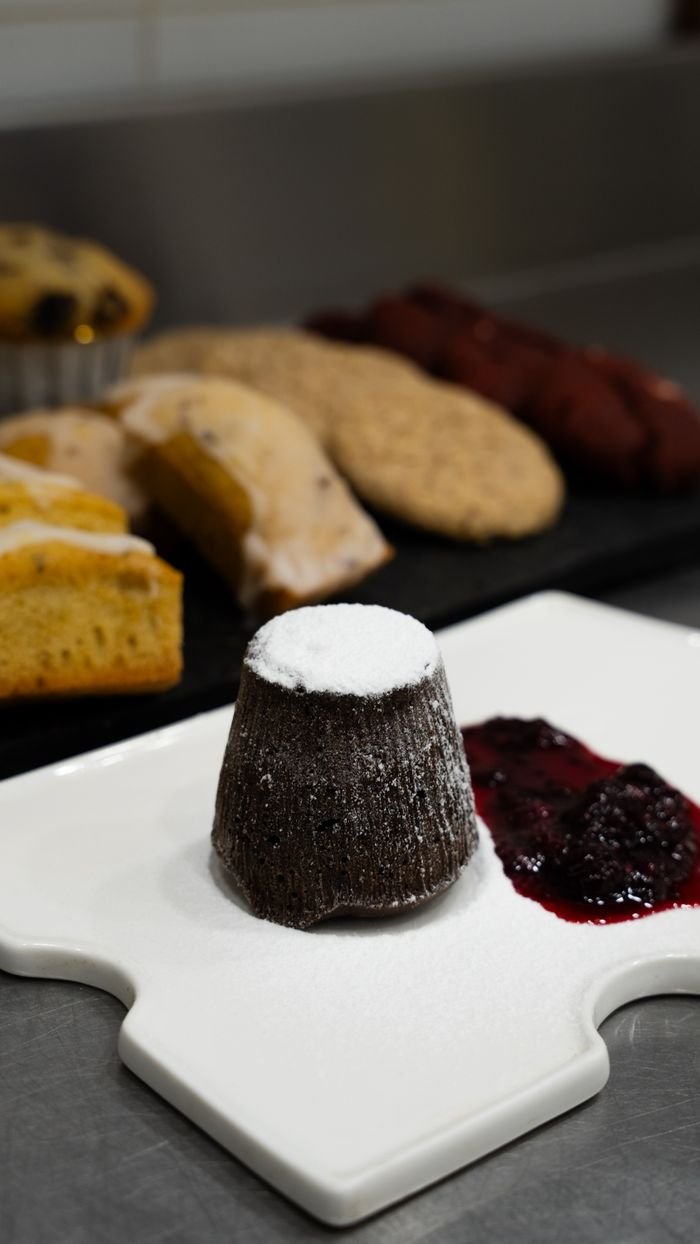social-feed-img-02 Assorted desserts including chocolate lava cake and fruit compote, presented on a white plate in a kitchen setting.
